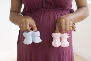 Pregnant African woman holding boy's and girl's baby shoes