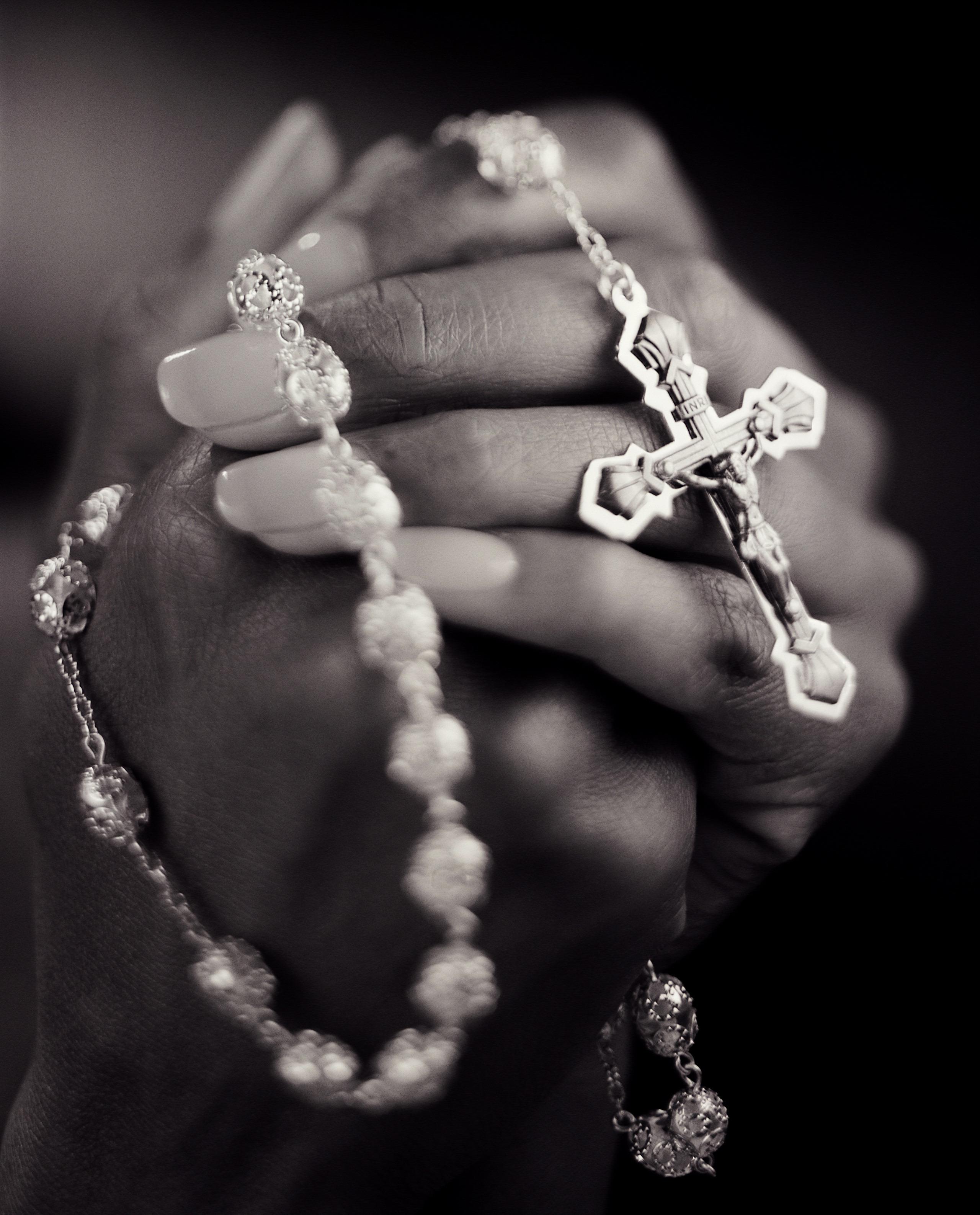 Young woman clasping rosary, close-up (B&W)