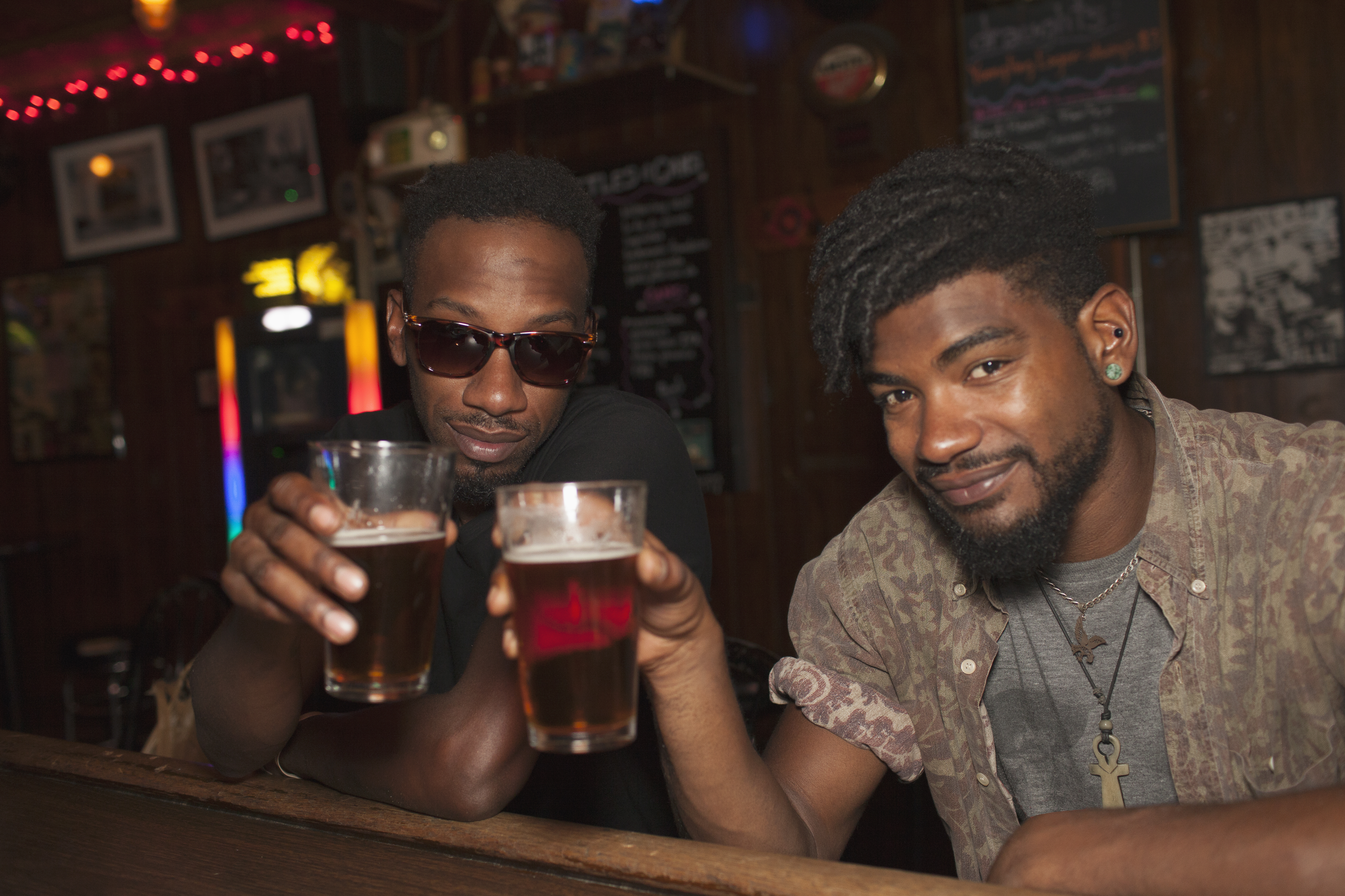 Two young men toasting at a bar.