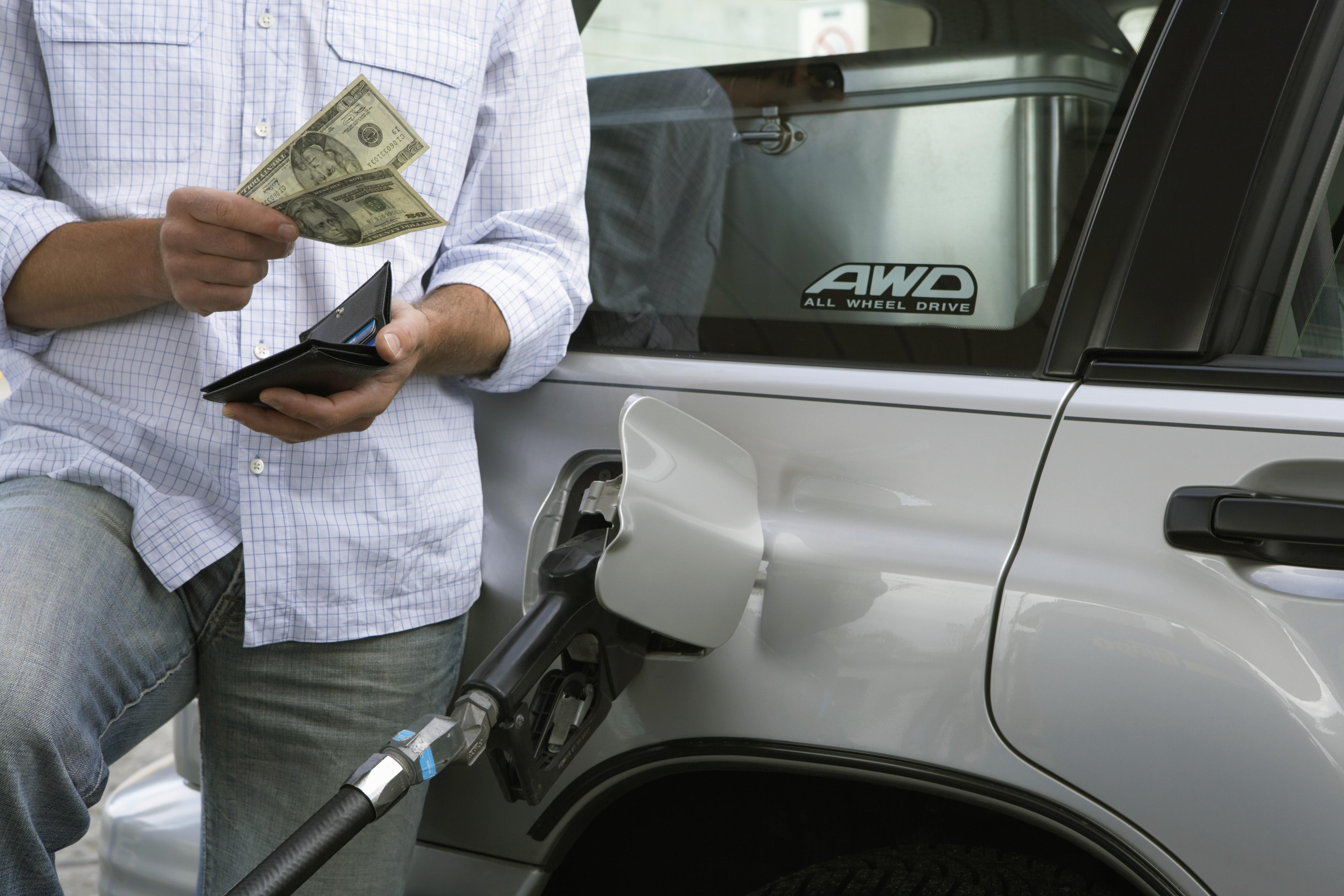 Man removing bank notes from wallet while refuelling car, mid section