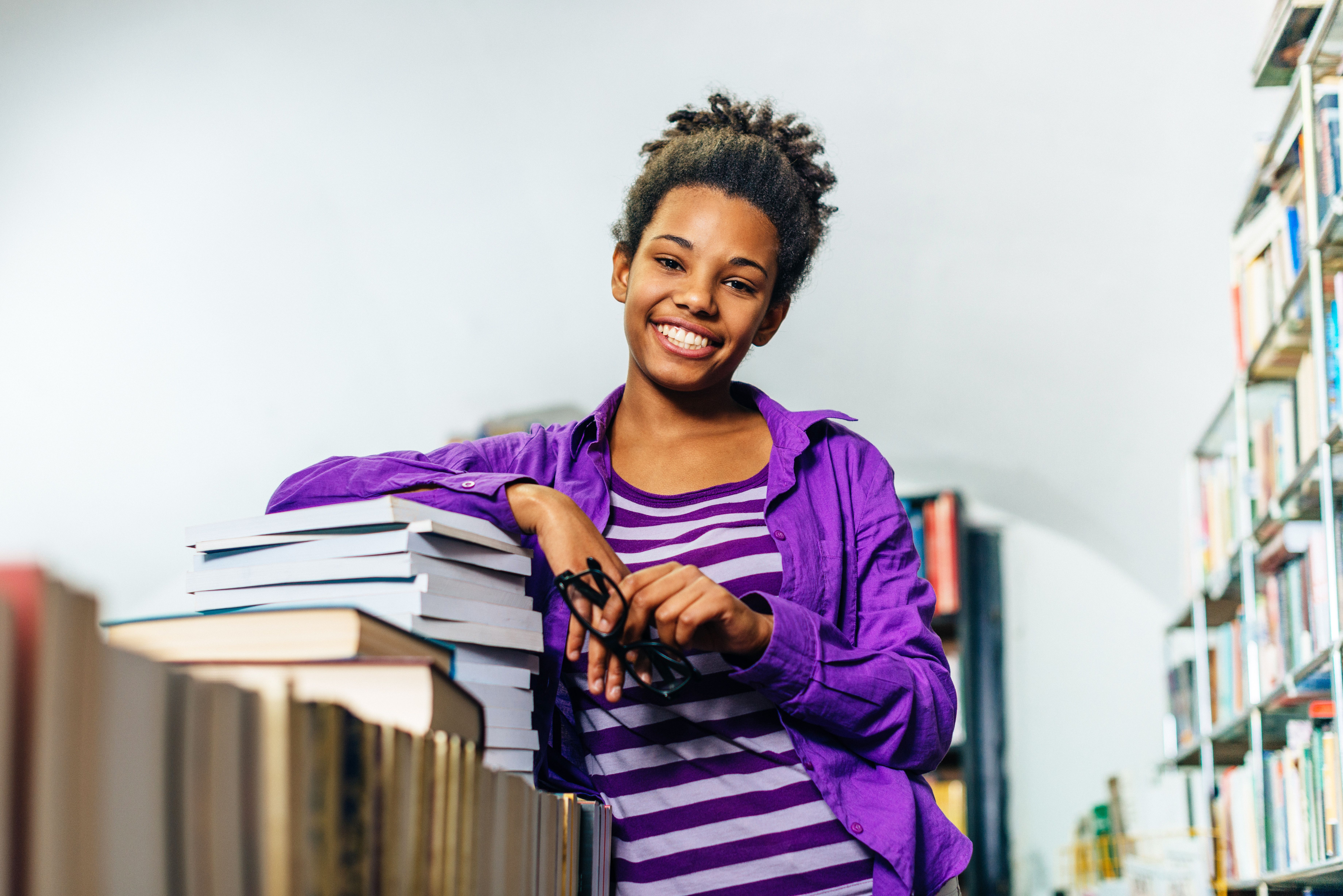 Pensive black girl in library posing with books