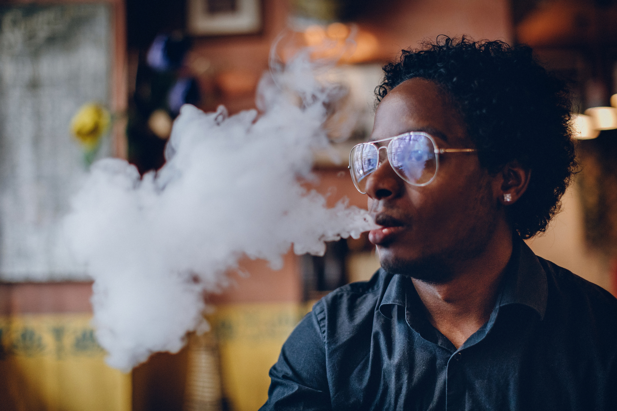 Young man smoking electronic cigarette in pub