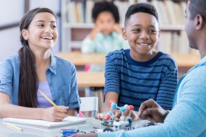 Two preteen students listen to Chemistry teacher define an atom