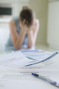 woman head in hands with a stack of unpaid bills