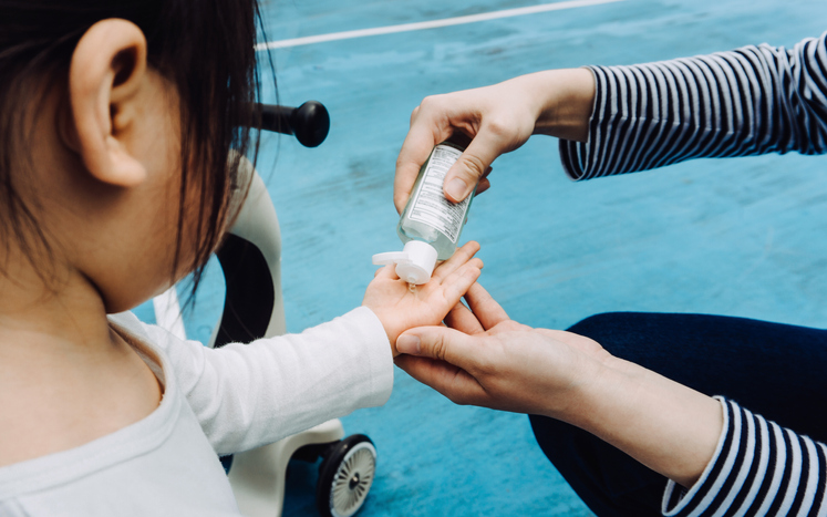 Young mother squeezing hand sanitizer onto little daughter's hand in the playground to prevent the spread of viruses