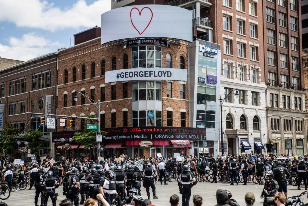 Protesters confront police officers standing in the middle...
