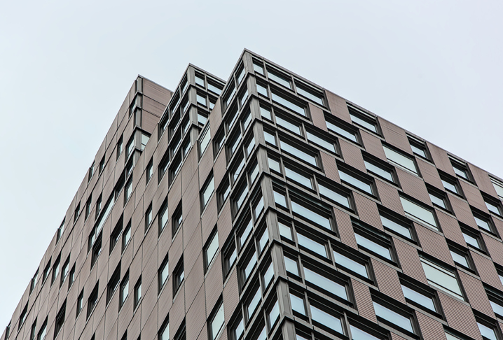tall residential building tower (looking up at high rise apartment against dark gray overcast sky) windows reflecting light, skyscraper, home, coop, condo, real estate, new construction