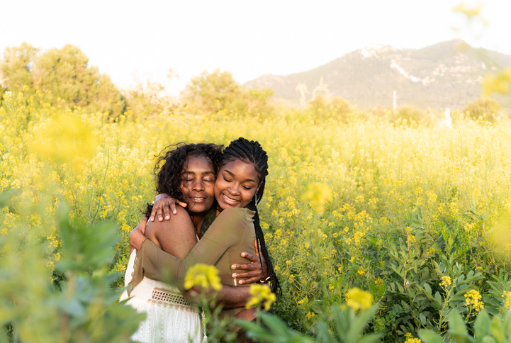Mother and daughter black women embracing in a field of yellow flowers