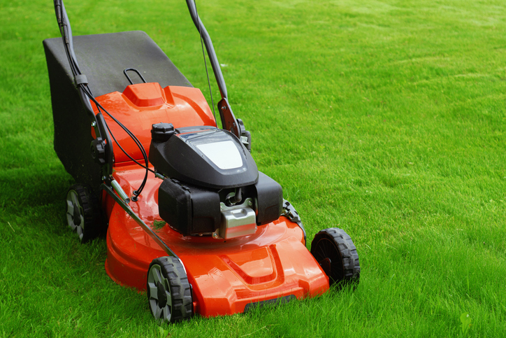 Close-up of a red lawn mower on fresh green grass. Concept gardening, landscaping, and lawn maintenance.