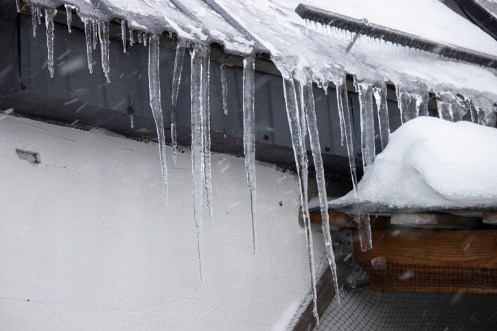 Sharp icicles hanging from the roof during snowfall. Winter weather.
